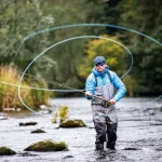 A man engaging in fly fishing, standing in water with a fishing rod at Roxburghe Hotel Golf & Spa Ltd.