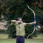 Man practicing archery at SCHLOSS Roxburghe's target range under expert instruction.