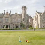 Sunny lawn in front of a large stone building, perfect for a game of croquet at Roxburghe Hotel.