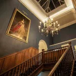 Elegant staircase with chandelier in 12.18. Roxburghe Hotel, showcasing timeless design and luxury.