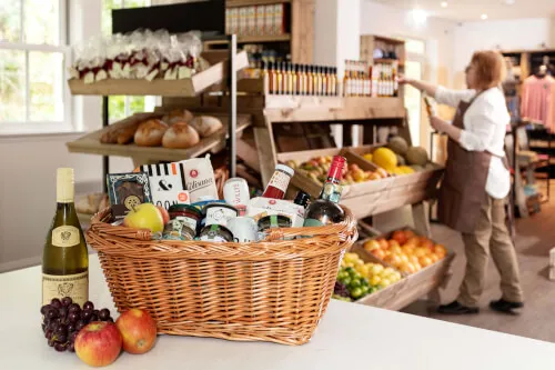 Wicker basket filled with fruits and goodies in a shop with a woman arranging products.