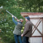 A woman aiming a shotgun with an instructor at Roxburghe Hotel Golf & Spa shooting range.