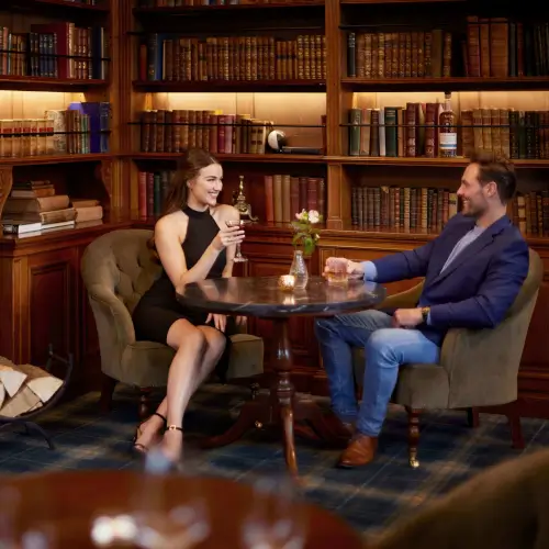 Couple enjoying drinks in a cozy library-style bar at Roxburghe Hotel Golf & Spa.