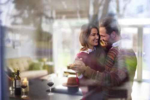 A happy couple dancing together with a wine glass on the table.