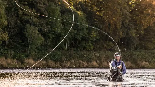 A man fly fishing in the river, showcasing the tranquility of nature.