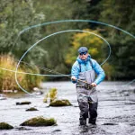 Man fishing in a river with a fly rod, showcasing the beauty of nature.