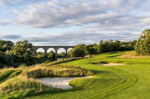 A scenic view of Roxburghe Golf Course with a stone bridge in the background.