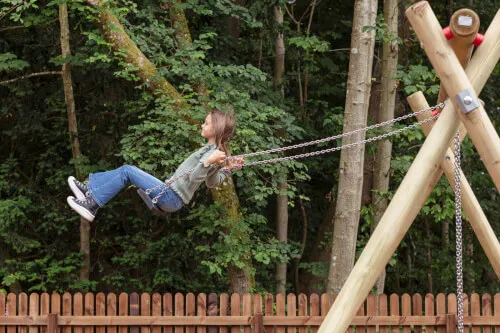 A girl enjoying a swing in a forested playground at Roxburghe Hotel Golf & Spa.