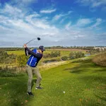 Golfer swinging at the Roxburghe Hotel Golf & Spa amidst scenic views.