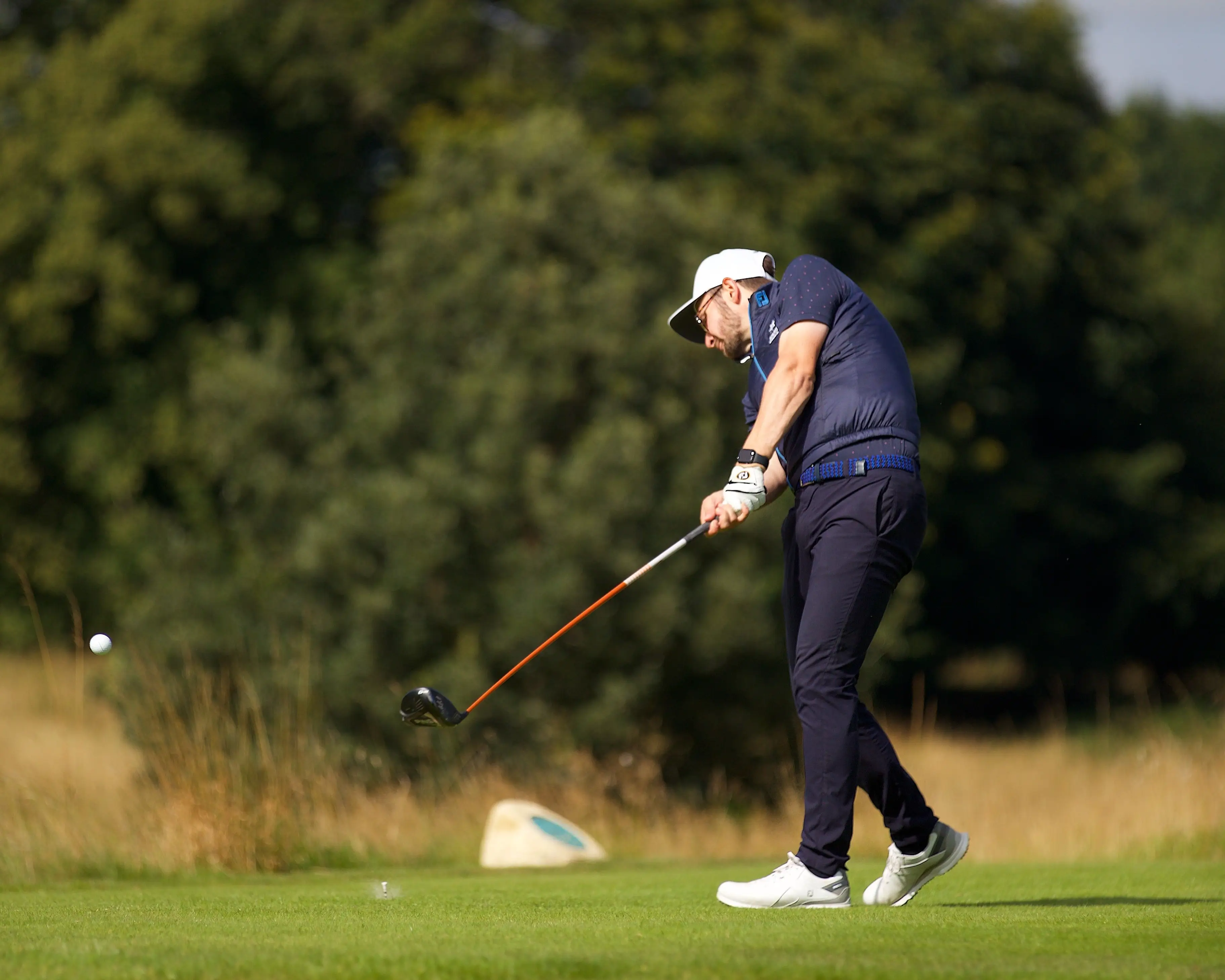 Golfer swinging on a golf course with trees in the background.