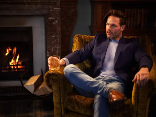 A man enjoying a drink by the fireplace in a sophisticated hotel setting.