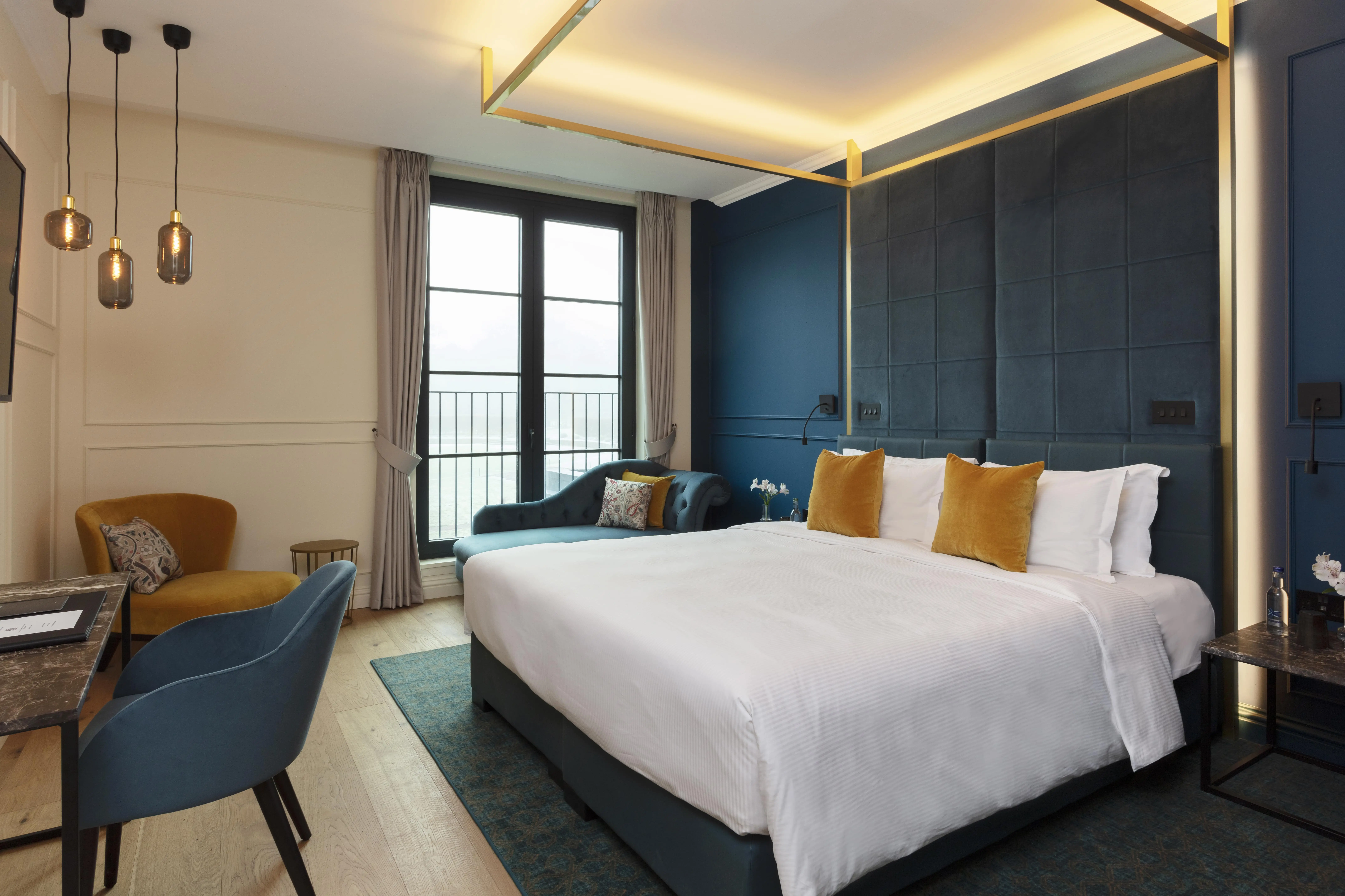 Stylish hotel room with a bed, blue chair, and large window at Roxburghe Hotel Golf & Spa.