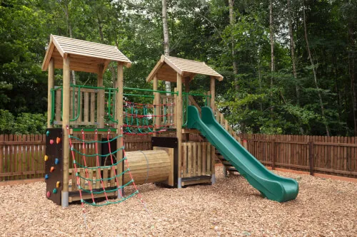 Wooden playground structure with slides and climbing features in a forested area.