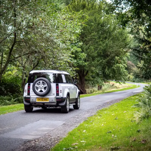 A silver SUV driving along a tranquil road surrounded by lush trees in Scotland.