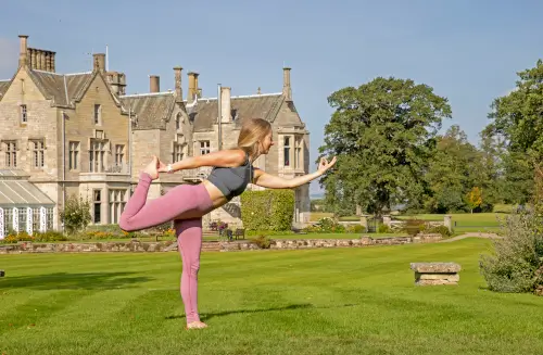 Woman practicing yoga at Roxburghe Hotel Golf & Spa surrounded by beautiful landscapes.